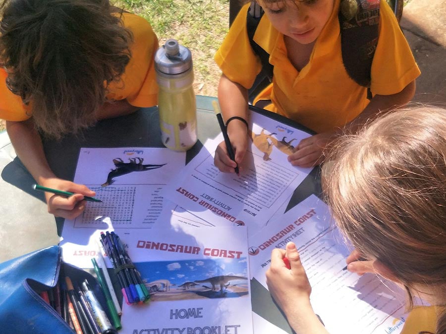 School students completing dinosaur themed activity books